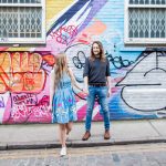 Couple holding hands against colourful wall with street art