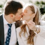 Bride holding out her hand to show her new wedding ring while kissing groom